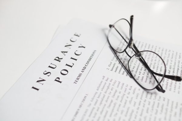 insurance policy contract with spectacles on white table. Close up view.
